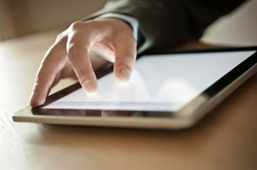 A man has his two fingers on a tablet enlarging the scree font.