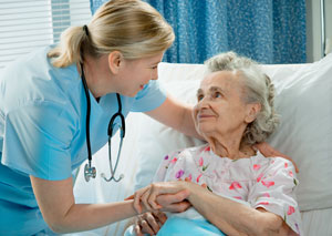 Female Nurse taking care of elderly female patient that is sitting up in a swing bed . They are smiling at each other.