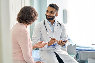 Female Patient is next to a male Physician who is taking down notes on a clipboard as she talks about her health.