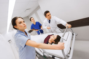 Three Medical Professionals rushing a female patient down the hospital hallway to the Emergency Department.